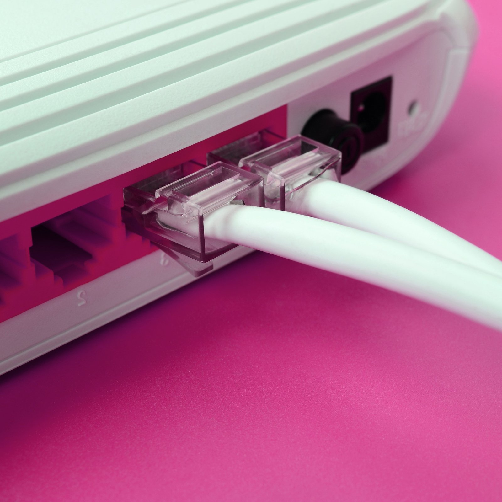 The Internet cable plugs are connected to the Internet router, which lies on a bright pink backgrou